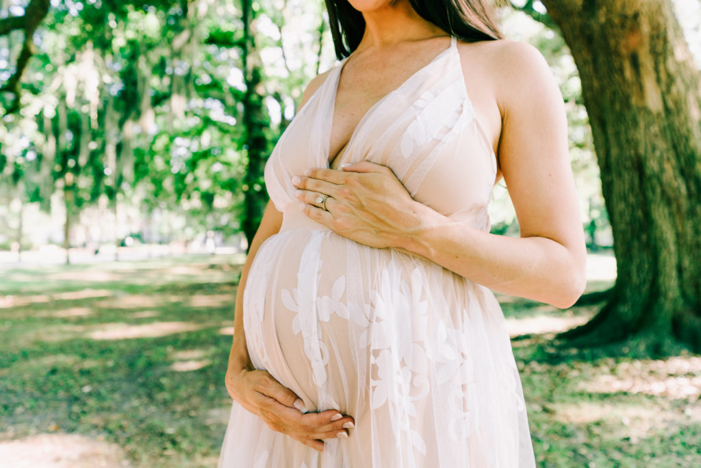 Pregnant woman in while flowy dress holding baby bump. Doula Savannah GA